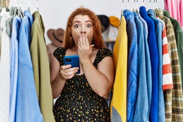 Sticker - Young redhead woman searching clothes on clothing rack using smartphone covering mouth with hand, shocked and afraid for mistake. surprised expression