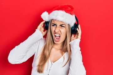 Canvas Print - Beautiful hispanic woman wearing christmas hat and headphones angry and mad screaming frustrated and furious, shouting with anger. rage and aggressive concept.