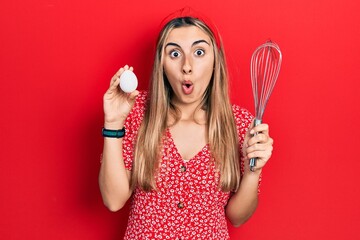 Canvas Print - Beautiful hispanic woman holding egg and baker whisk afraid and shocked with surprise and amazed expression, fear and excited face.