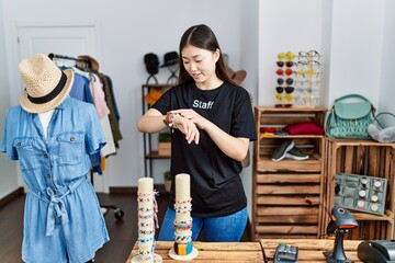 Poster - Young asian woman working as manager at retail boutique checking the time on wrist watch, relaxed and confident