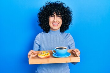 Sticker - Young middle east woman holding tray with doughnut and cup of coffee smiling with a happy and cool smile on face. showing teeth.