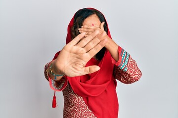 Poster - Middle age hispanic woman wearing tradition sherwani saree clothes covering eyes with hands and doing stop gesture with sad and fear expression. embarrassed and negative concept.