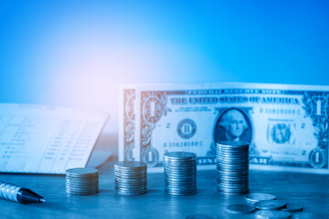 Stack of money coin and dollars banknotes on wood desk with calculator and pen. Business and financial concept with blue filter. 