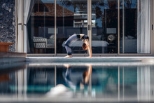 Young Slim Flexible Model Wearing Sports Tight Clothing And Standing On The Bridge Doing Yoga On A Yoga Mat Next To The Pool. Flexibility Concept