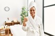 © Krakenimages.com - Young brunette woman wearing towel and bathrobe standing at beauty center doing happy thumbs up gesture with hand. approving expression looking at the camera showing success.