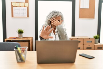 Poster - Middle age businesswoman sitting on desk working using laptop at office covering eyes with hands and doing stop gesture with sad and fear expression. embarrassed and negative concept.