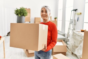 Wall Mural - Middle age grey-haired woman smiling confident holding package at new home