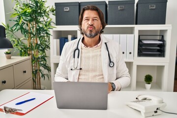 Canvas Print - Handsome middle age doctor man working at the clinic looking at the camera blowing a kiss on air being lovely and sexy. love expression.