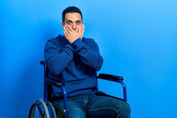 Sticker - Handsome hispanic man with beard sitting on wheelchair shocked covering mouth with hands for mistake. secret concept.