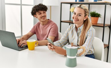 Poster - Young couple using laptop and smartphone drinking coffee at home.