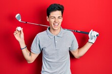 Young Hispanic Man Holding Golf Ball Winking Looking At The Camera With Sexy Expression, Cheerful And Happy Face.
