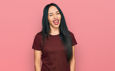 Young hispanic girl wearing casual t shirt winking looking at the camera with sexy expression, cheerful and happy face.