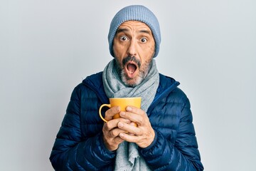 Poster - Middle age hispanic man wearing winter scarf and drinking a cup of hot coffee afraid and shocked with surprise and amazed expression, fear and excited face.