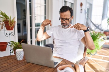 Sticker - Middle age man using computer laptop at home pointing down looking sad and upset, indicating direction with fingers, unhappy and depressed.