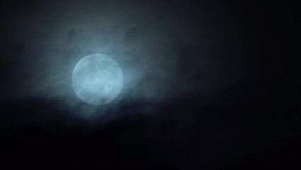 bright white full moon rising in the sky - dark mystical clouds passing in front while moon slowly m