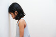 Side view of Asian kid showing sad expression with her head on the wall