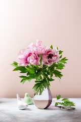 Wall Mural - Bouquet of pink flowers of tree peony in glass vase on beige background. Still life.