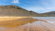 Goldene Strand der Westfjorde mit rötlichem Sand, grünen Wiesen im Vordergrund und seichten, dunstigen Hügeln im Hintergrund.