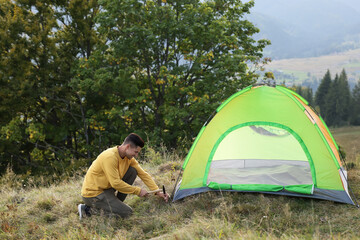 Canvas Print - Man setting up camping tent on hill