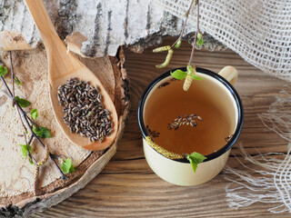 Birch buds and twigs with leaves in a wooden spoon, herbal tea in a mug on a wooden background, flat layout. Healing betula plant for use in medicine, homeopathy and cosmetology