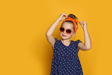 Wall Mural - Cute little girl wearing stylish bandana and sunglasses on orange background, space for text