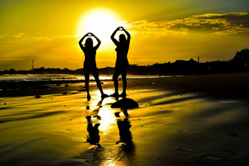 silhouette of 2 young women on the beach at sunrise