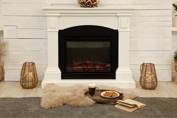 Poster - Open book, hot drink and cookies near decorative fireplace in living room. Cozy home atmosphere