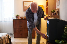 Senior Man In Casualwear Bending By Tv Set And Pushing Button On Panel Below Screen While Switching It On Or Off