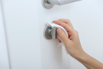 Cleaning door handles with an antiseptic wet wipe and gloves. Sanitize surfaces prevention in hospital and public spaces against corona virus. Woman hand using towel for cleaning home room door link