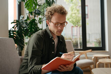 Pensive student studying, learning language sitting at workplace.  Education concept. Portrait of young handsome man writer wearing stylish eyeglasses taking notes working from home   