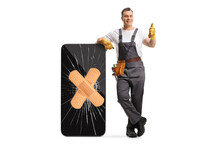 Full length portrait of a repairman leaning on a broken smartphone with bandage and showing thumbs up