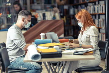 Wall Mural - Two students in college library studying during the period of coronavirus.	
