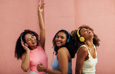 Wall Mural - Three young women with curly hair wearing headphones and dancing