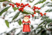 Santa Claus Ornament Hanging From Snow Covered Holly Branch With Red Berries