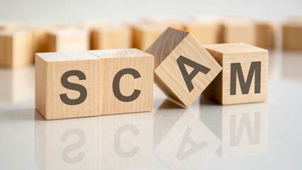 Sticker - four wooden blocks with the letters scam on the bright surface of a gray table, business concept