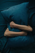 A young unrecognizable woman hides under a pillow. The woman presses the pillow tightly against her face. Concept of depression or mental health problems.