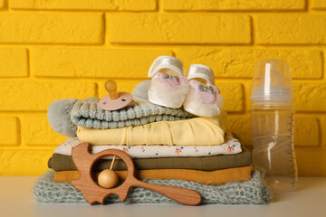 Baby clothes, toy and accessories on white table near yellow brick wall