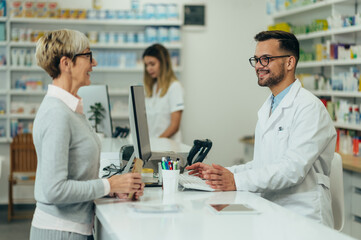 Wall Mural - Young male pharmacist giving prescription medications to senior female customer in a pharmacy