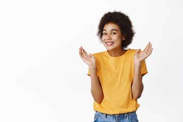 Oops. Smiling silly black girl showing shrugging pose and looking guilty, standing in yellow tshirt over white background