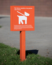 An Orange Sign Requests Visitors In Spanish To Keep Their Dogs On A Leash While Visiting A Park In Los Angeles, CA.