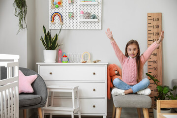 Wall Mural - Happy little girl sitting on ottoman at home