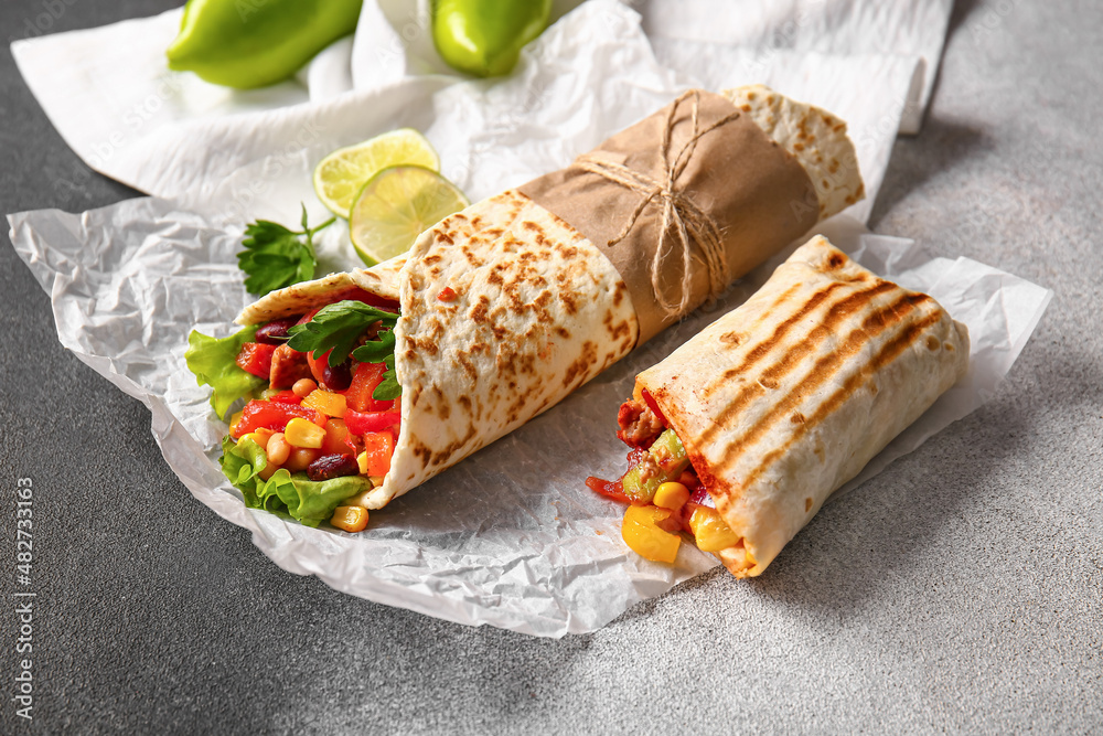 Parchment with delicious burritos and lime on grey background