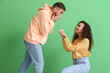 Young woman proposing to her shocked boyfriend on color background