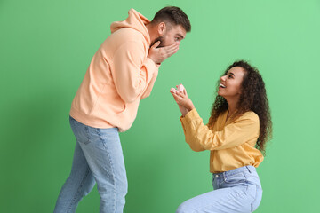 Canvas Print - Young woman proposing to her shocked boyfriend on color background