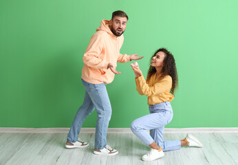 Wall Mural - Young woman proposing to her shocked boyfriend on color background