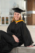 © Nathan Allred - attractive blond female college graduate in cap and gown sitting in front of university building and smiling