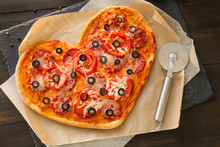Board With Tasty Heart-shaped Pizza And Knife On Black Wooden Background. Valentine's Day Celebration