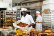 Professional African American baker working in bakehouse, carrying box with baked bread..