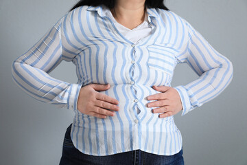 Wall Mural - Overweight woman in tight shirt on light grey background, closeup