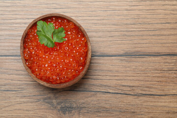 Bowl with delicious red caviar and parsley leaf on wooden table, top view. Space for text